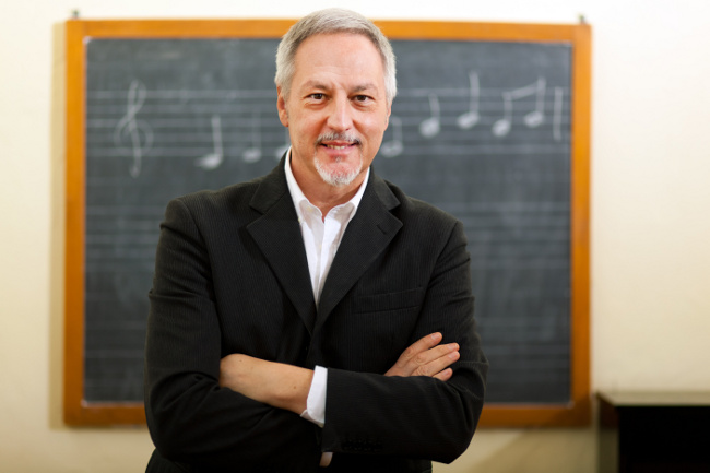 Featured image for "Music Lessons Domains" page on 251 group dotcom depicting male music teacher standing confidently in front of blackboard with arms folded.